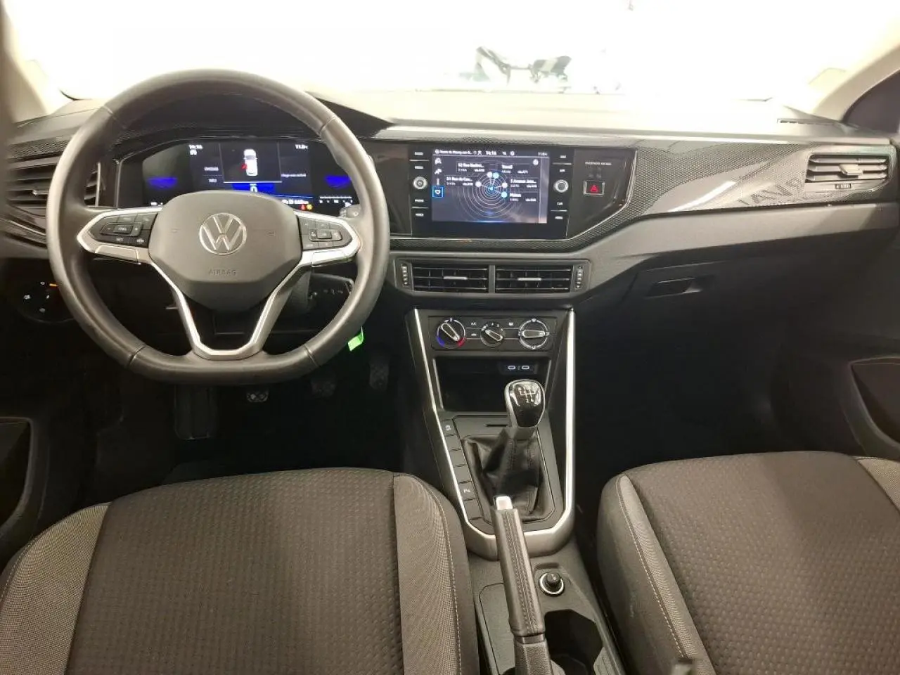 Intérieur avant de Volkswagen Polo gris clair 2023, volant cuir multifonction et console centrale avec boîte manuelle.