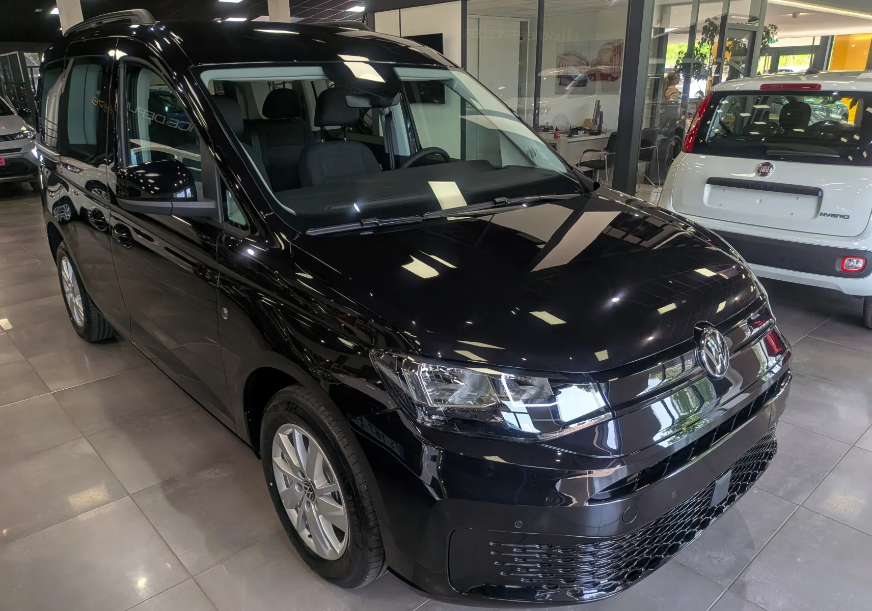 Volkswagen Caddy noir vue 3/4 avant droit en intérieur, avec phares LED et jantes alliage visibles.