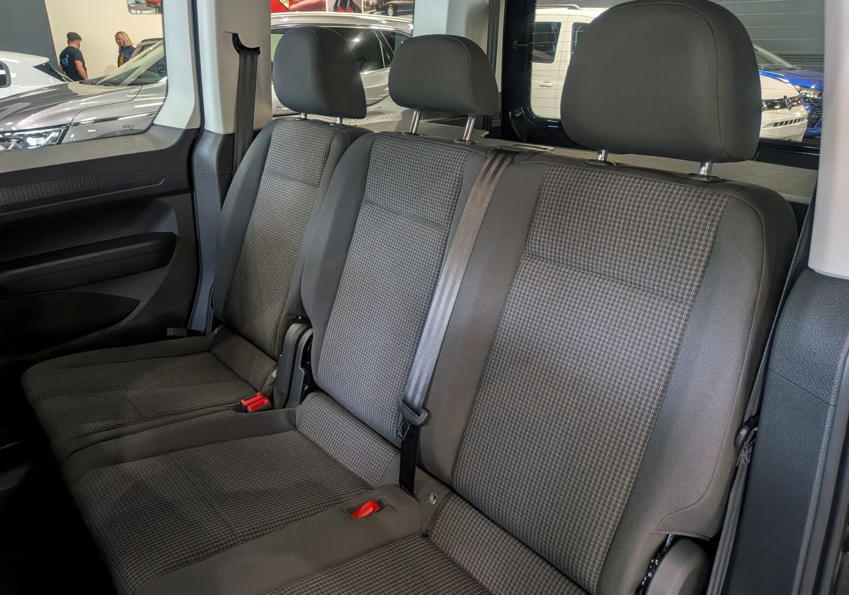 Vue intérieure des sièges arrière en tissu gris du Volkswagen Caddy 2.0 TDI noir, montrant trois appuie-têtes et ceintures de sécurité.