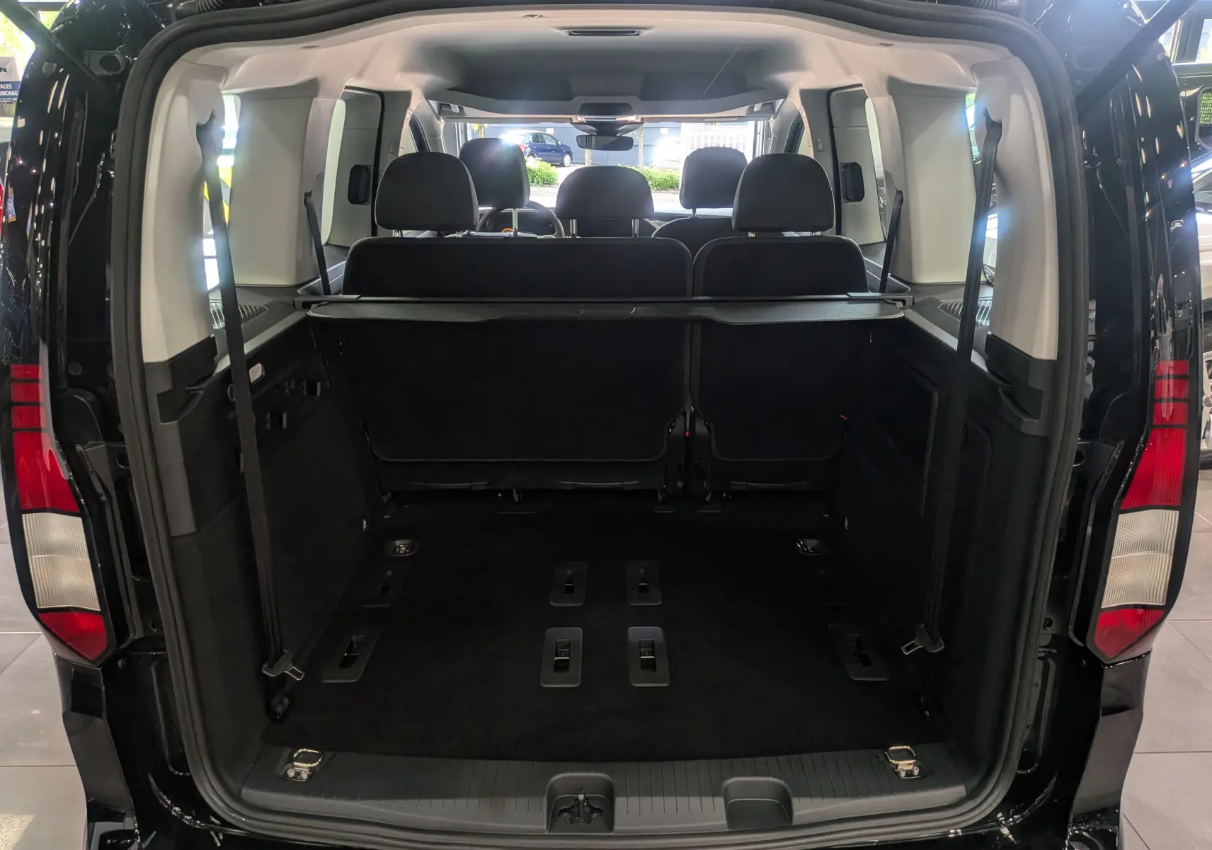 Vue arrière ouverte du Volkswagen Caddy noir 2025, montrant l'espace de chargement et les sièges arrière en tissu noir.