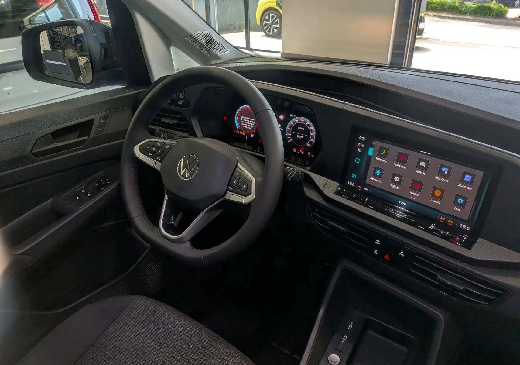 Vue intérieure côté conducteur du Volkswagen Caddy 2.0 TDI 2025, volant multifonction et écran tactile central visible.