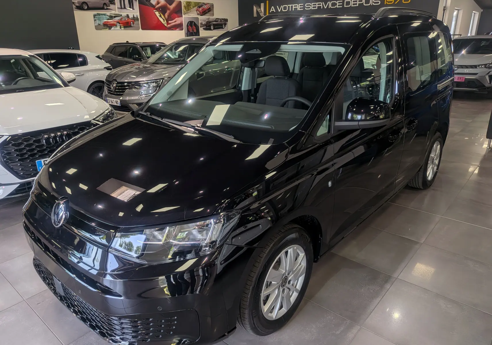 Volkswagen Caddy noir vue 3/4 avant droit en intérieur, avec jantes alliage et calandre brillante.