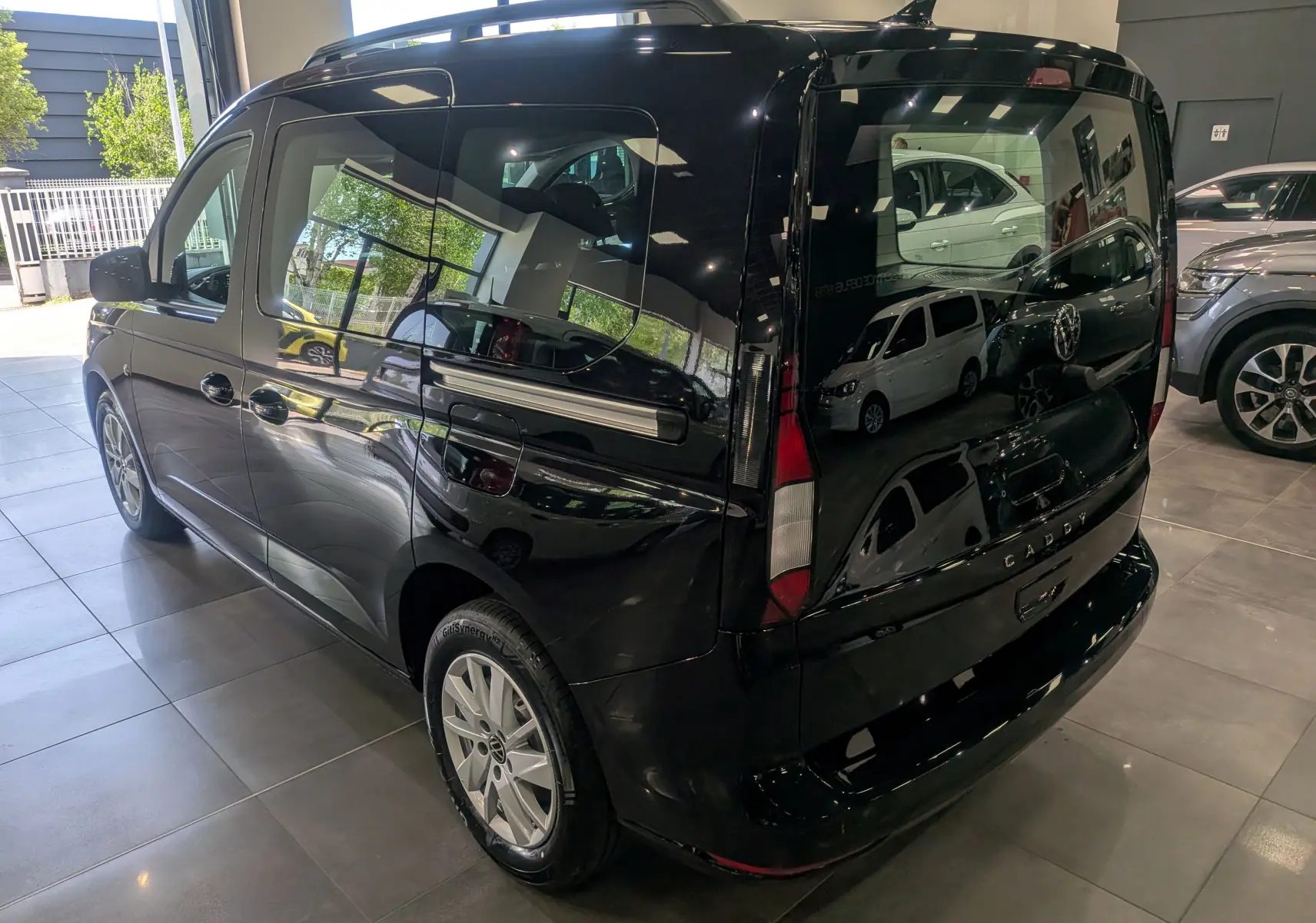 Volkswagen Caddy noir vue 3/4 arrière droit en intérieur, avec vitres teintées et jantes alliage.