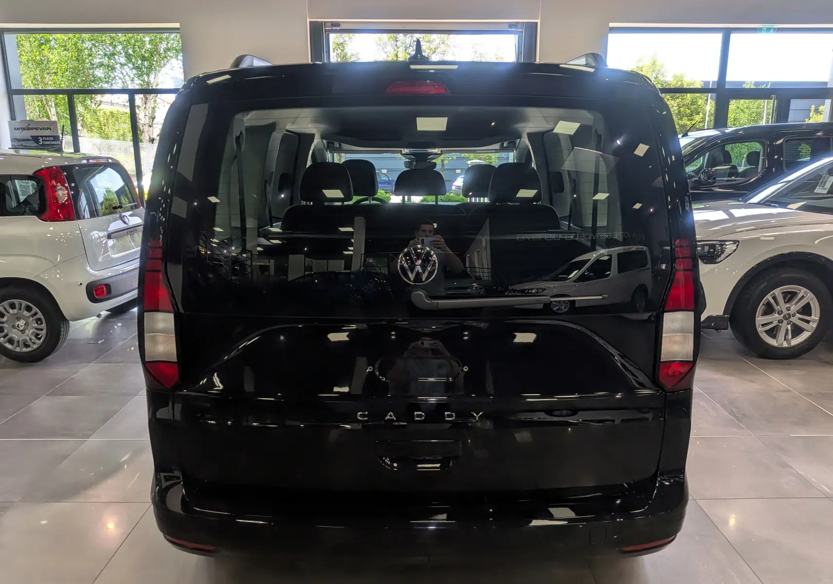 Vue arrière d'un Volkswagen Caddy noir 2025 dans un showroom, avec logo VW et vitres teintées.