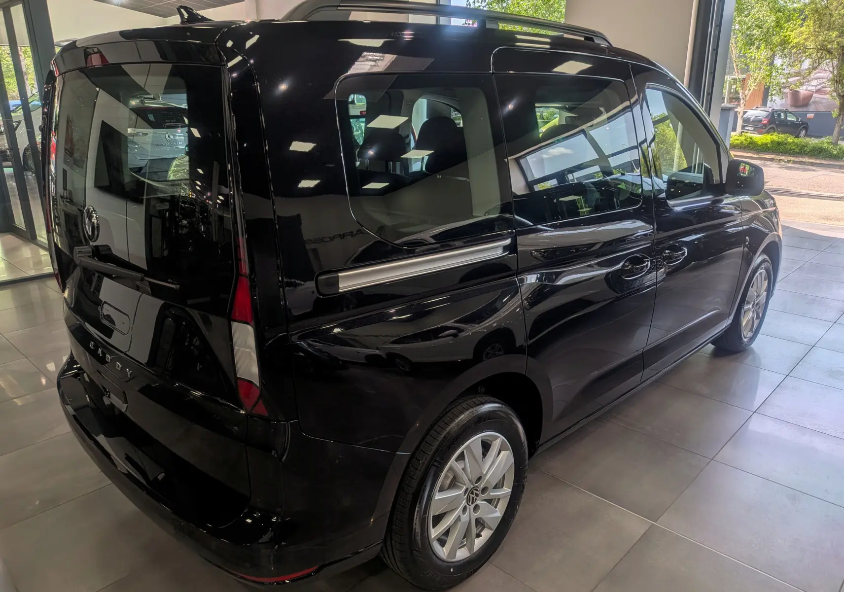 Vue 3/4 arrière droite d’un Volkswagen Caddy noir 2025 en showroom, avec vitres teintées et jantes alliage.