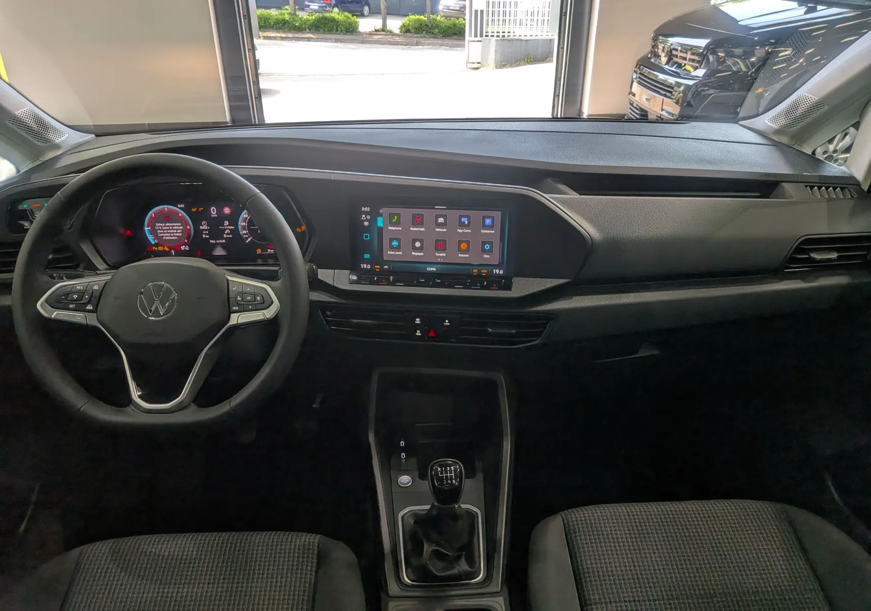 Vue intérieure frontale du tableau de bord noir du Volkswagen Caddy 2025 avec volant multifonction et écran tactile central.