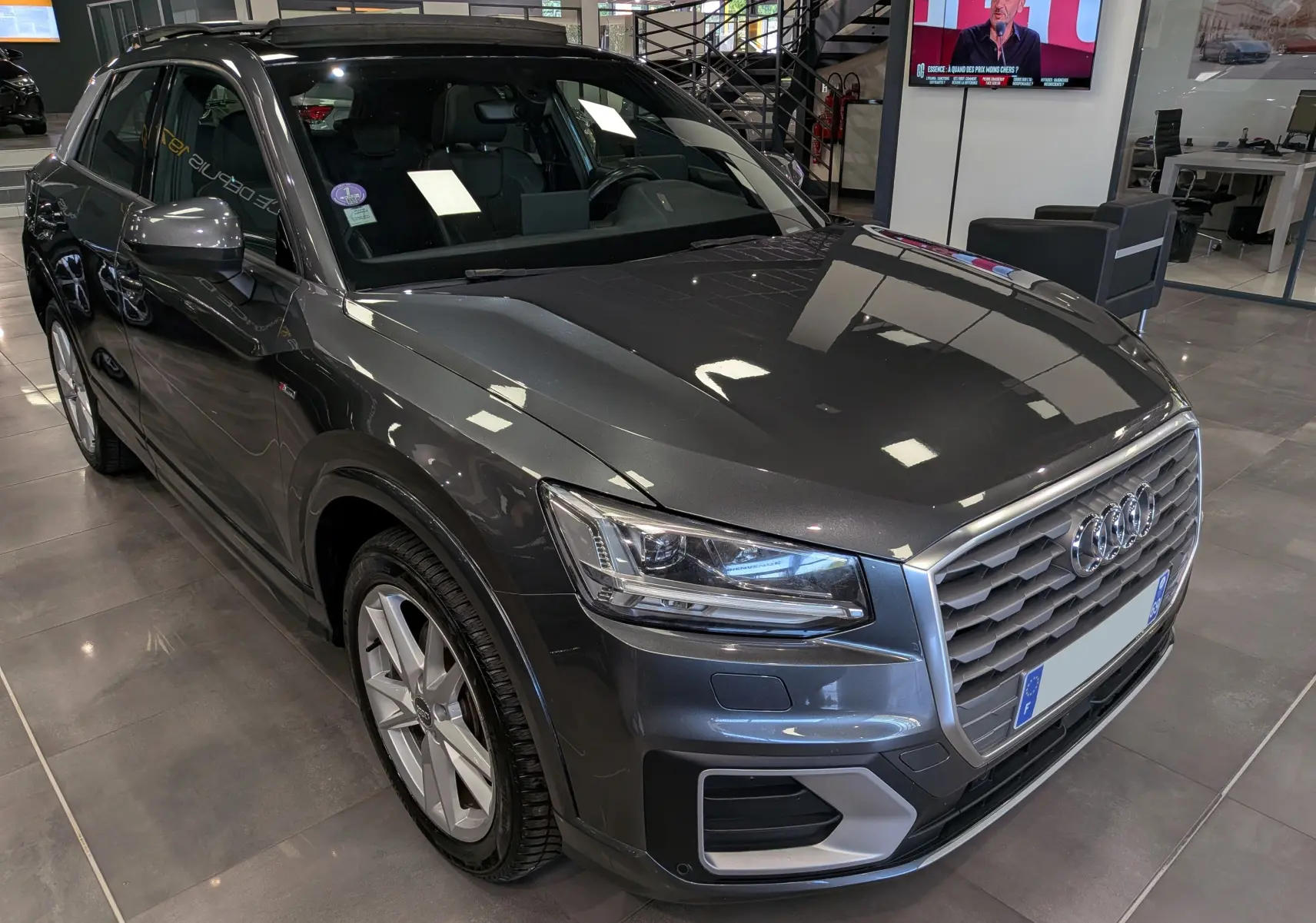 Audi Q2 gris métallisé vue 3/4 avant droit en intérieur, avec calandre hexagonale et jantes alliage 18 pouces.