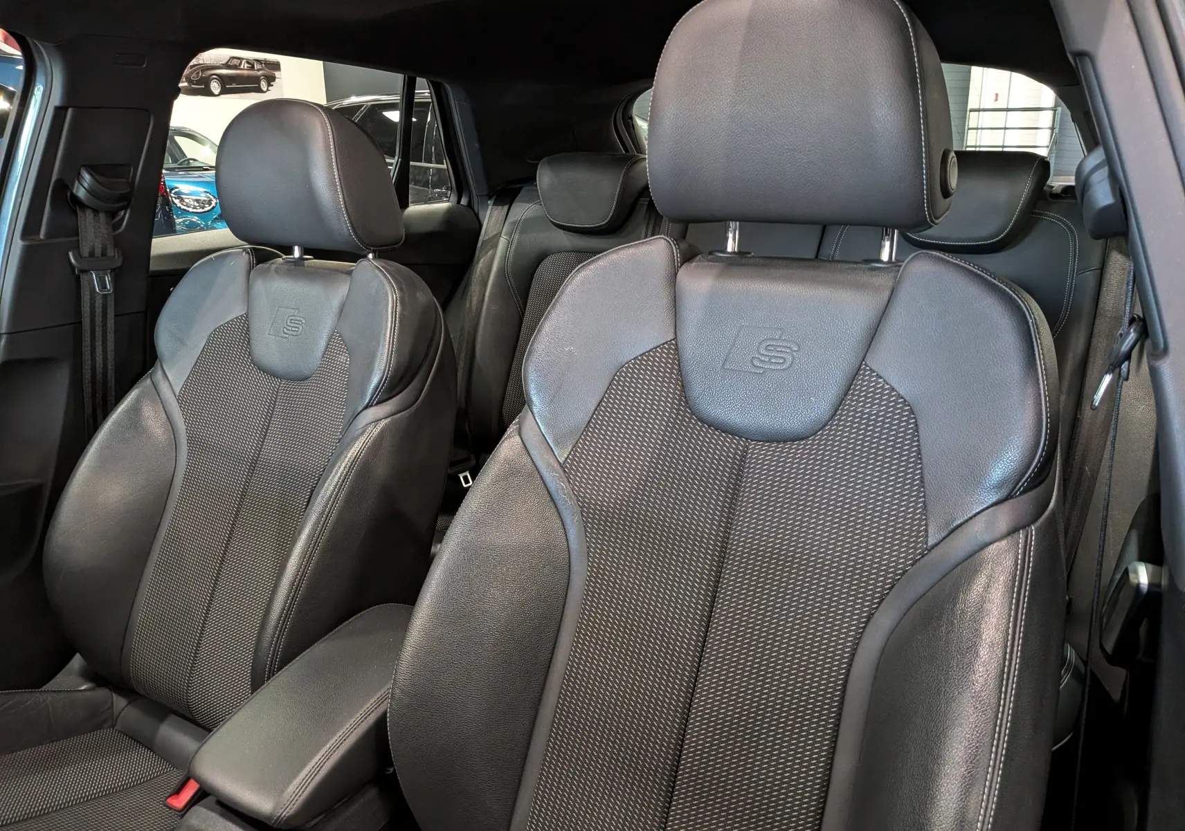 Gros plan sur les sièges avant en cuir noir avec logo S de l'Audi Q2 gris, intérieur sportif et élégant.