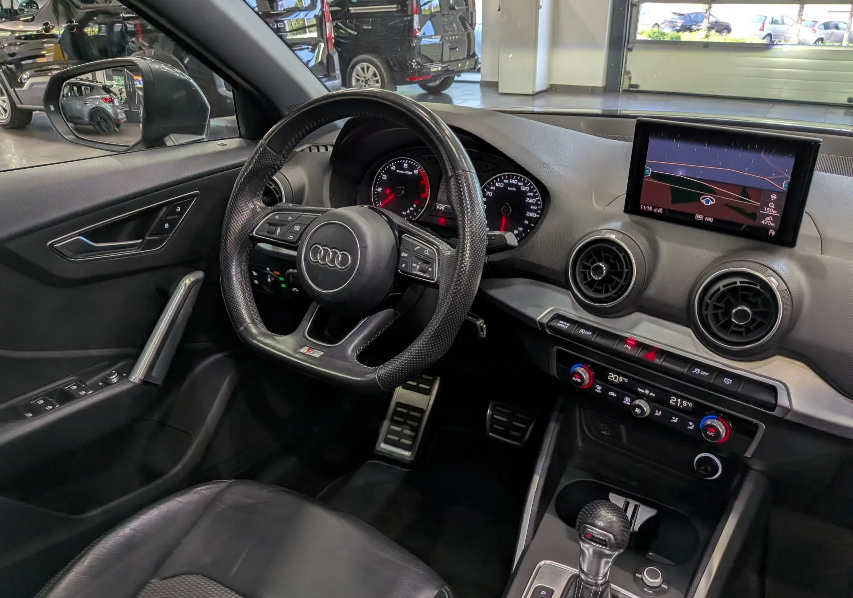 Vue intérieure côté conducteur de l'Audi Q2 1.4 TFSI S-Line 2017, volant sport, écran GPS et sellerie cuir noir.