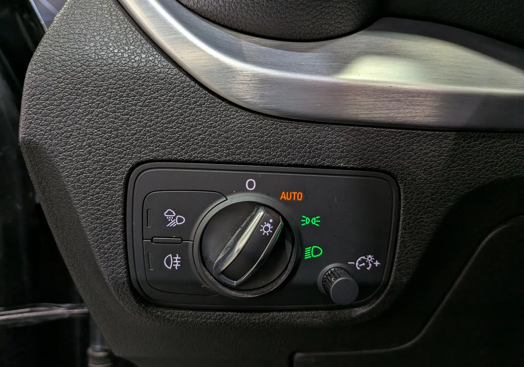 Gros plan sur le bouton de commande des phares avec éclairage automatique sur Audi Q2 gris, intérieur côté gauche.