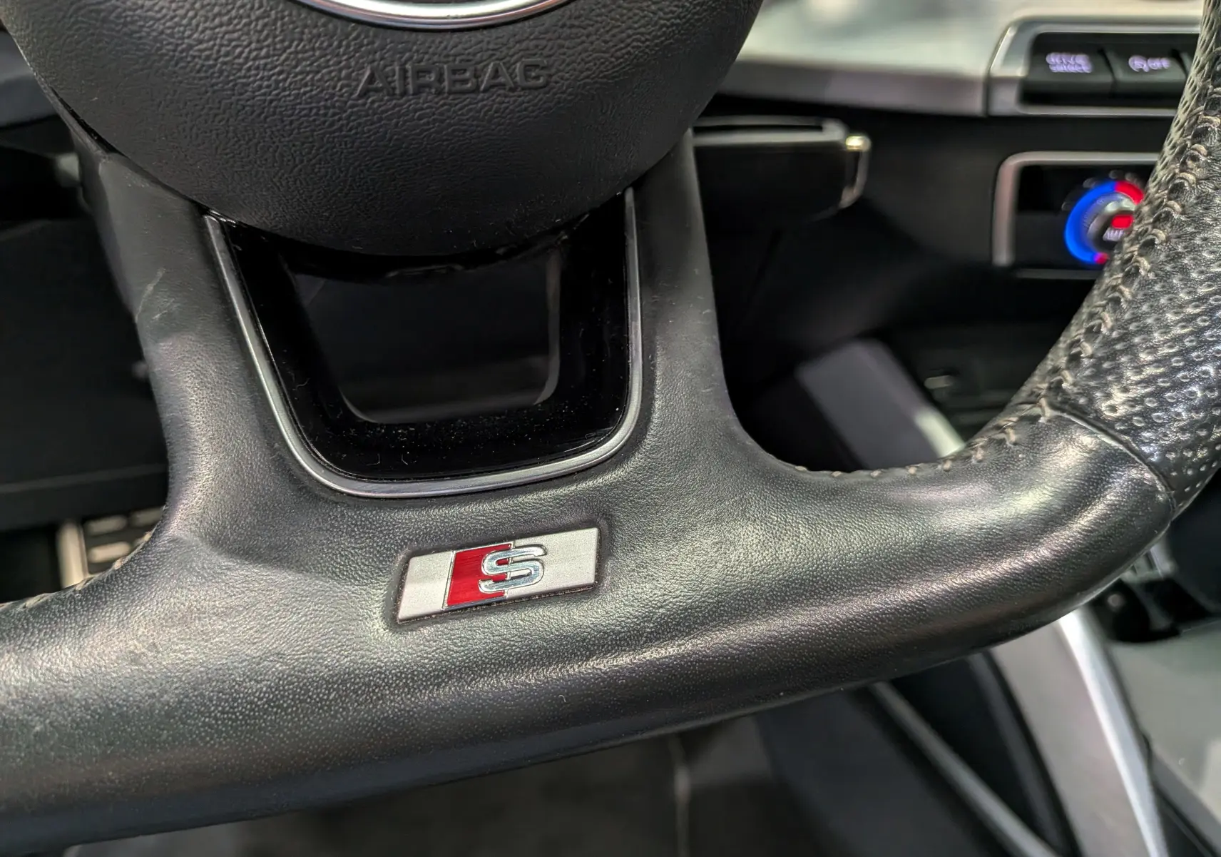 Gros plan sur le volant en cuir noir avec logo S de l'Audi Q2 1.4 TFSI S-Line, détails du tableau de bord en arrière-plan.