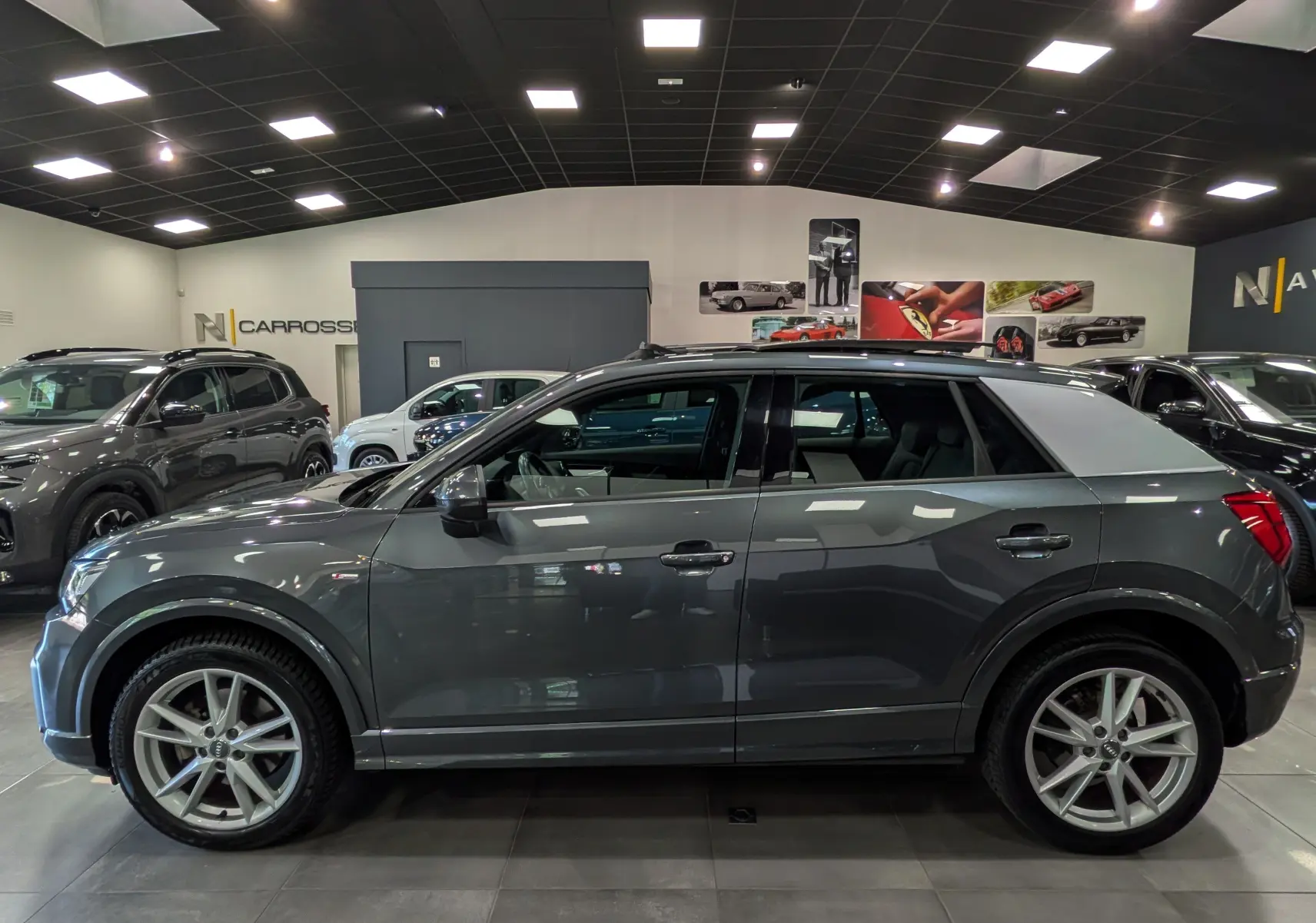 Audi Q2 gris vue de profil côté gauche en intérieur, avec toit contrasté argent et jantes alliage 18 pouces.
