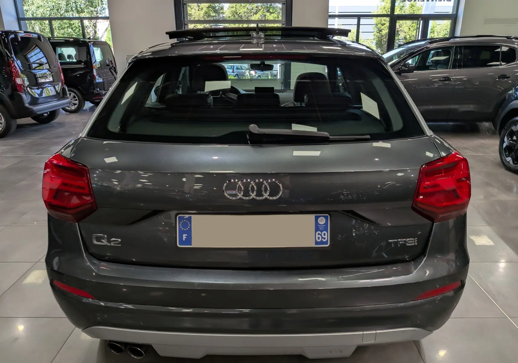 Vue arrière d'un Audi Q2 gris 2017 avec feux rouges et double sortie d'échappement visible en intérieur showroom.