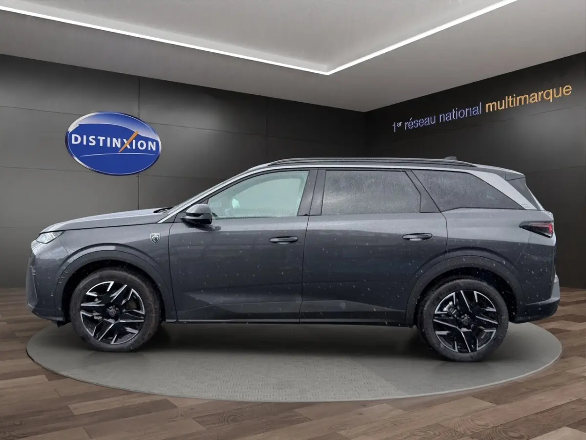 Vue de profil côté gauche d’un Peugeot 5008 gris foncé avec jantes noires et toit noir en showroom.