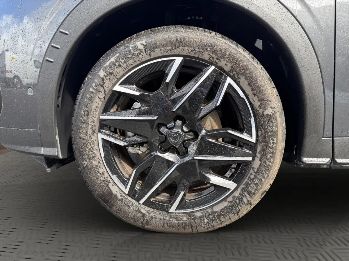 Gros plan sur la roue avant gauche d’un Peugeot 5008 gris foncé avec jante alliage noire et argentée, pneu boueux.