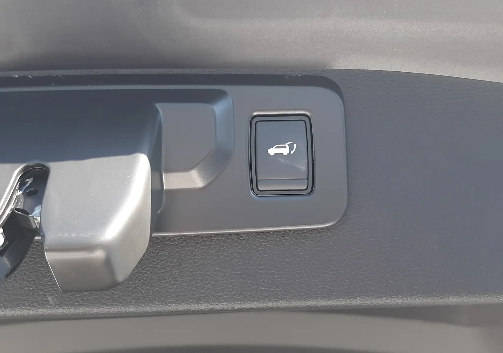 Bouton d'ouverture électrique du hayon sur la partie intérieure du coffre du Renault Symbioz gris cassiopée.