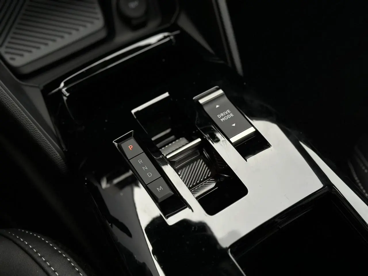 Gros plan sur la console centrale noire brillante de la Citroën C4 NV Hybrid 145 e-DSC6 Max avec sélecteur de vitesse et bouton Drive Mode.