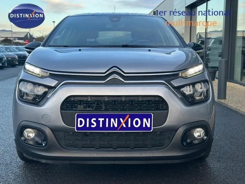 Vue frontale d'une Citroën C3 gris 2023 avec calandre noire et phares LED distinctifs, stationnée devant un showroom.