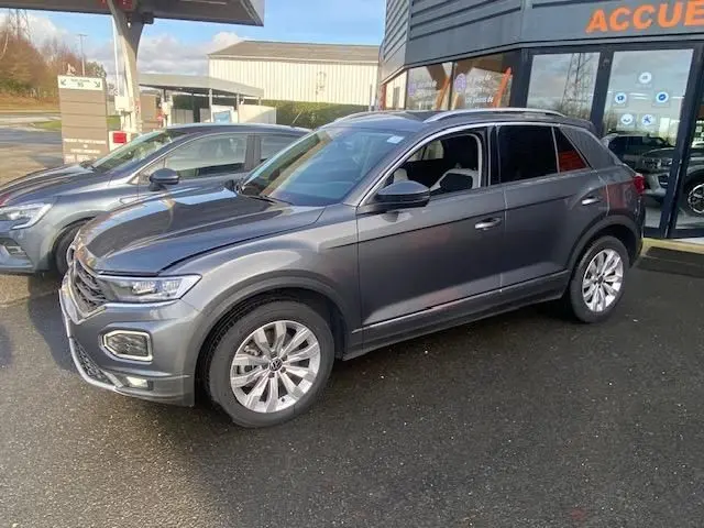 Volkswagen T-Roc TDI 150 DSG 7 Carat gris Indium en vue 3/4 avant droit, stationné devant un bâtiment.