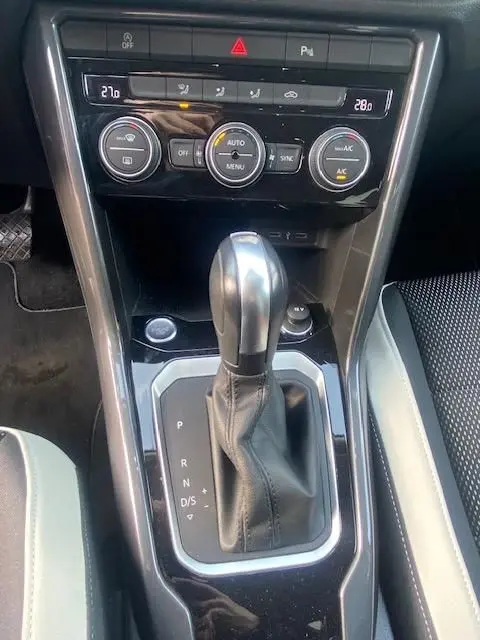 Gros plan sur la console centrale du Volkswagen T-Roc TDI 150 DSG 7 Carat, avec levier de vitesse automatique et commandes climatisation.