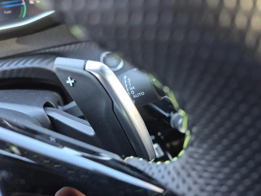 Gros plan sur la palette de changement de vitesse + du volant perforé d'une Peugeot 208 Hybrid 136 e-DCS6 GT blanc.