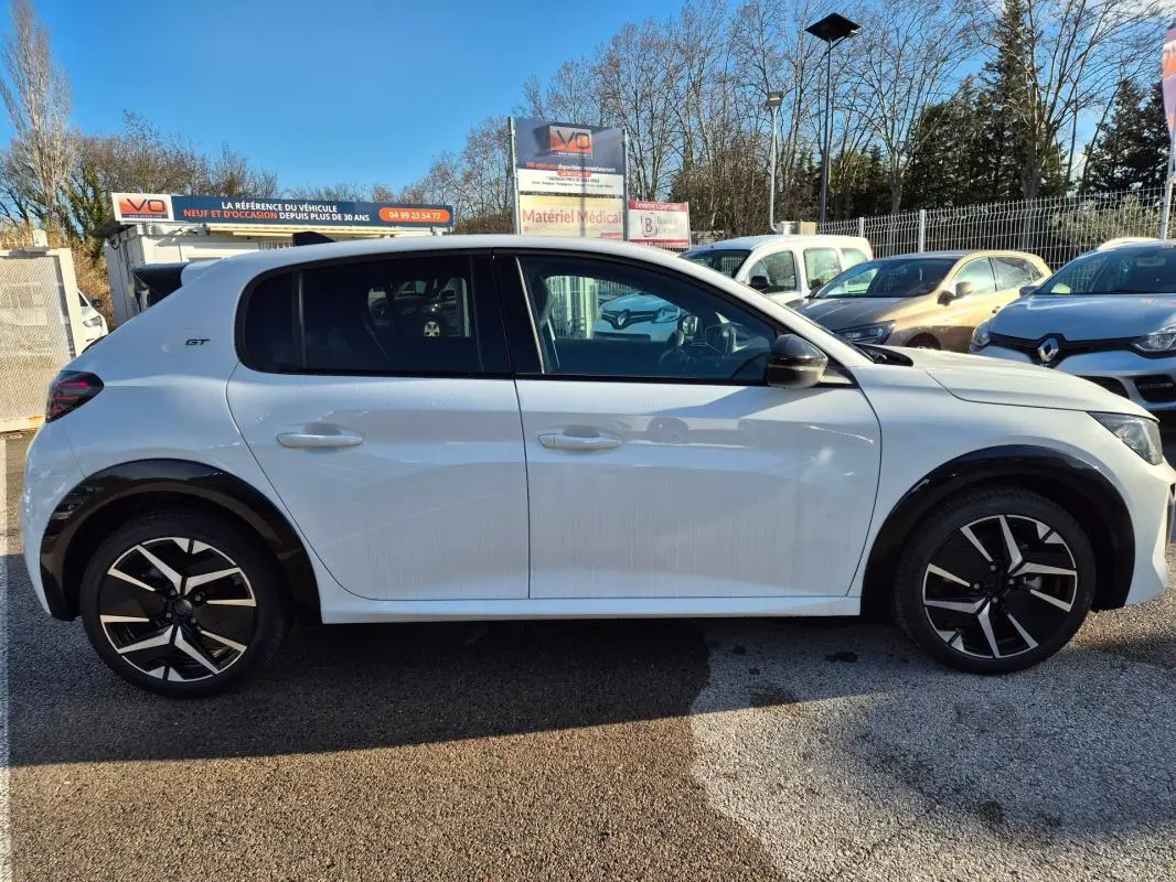 Profil droit d’une Peugeot 208 Hybrid 136 e-DCS6 GT blanche avec jantes alliage 17 pouces et logo GT sur l’aile arrière.