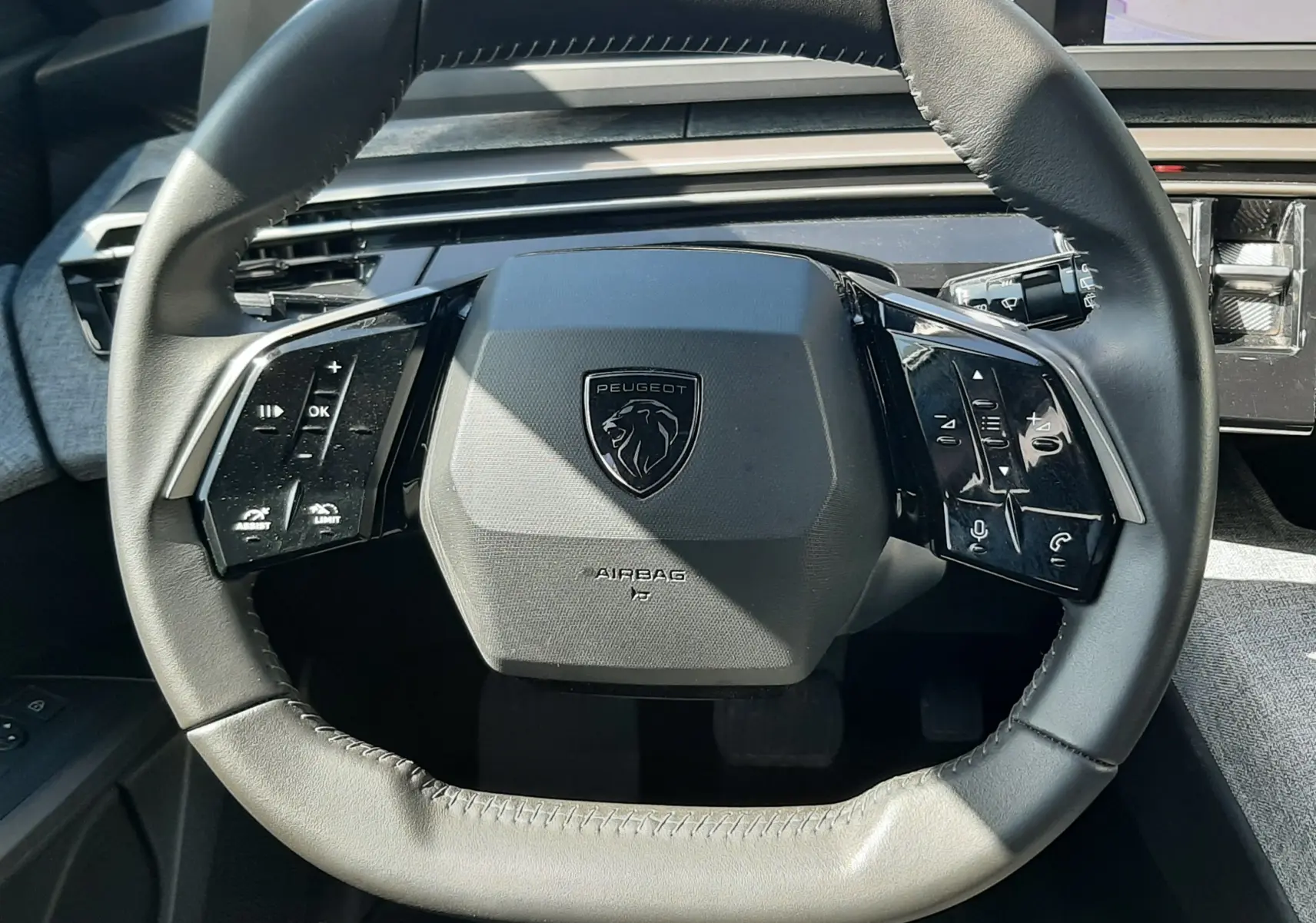 Vue rapprochée du volant cuir noir du Peugeot 5008 Hybrid 2025 avec commandes intégrées et tableau de bord numérique.