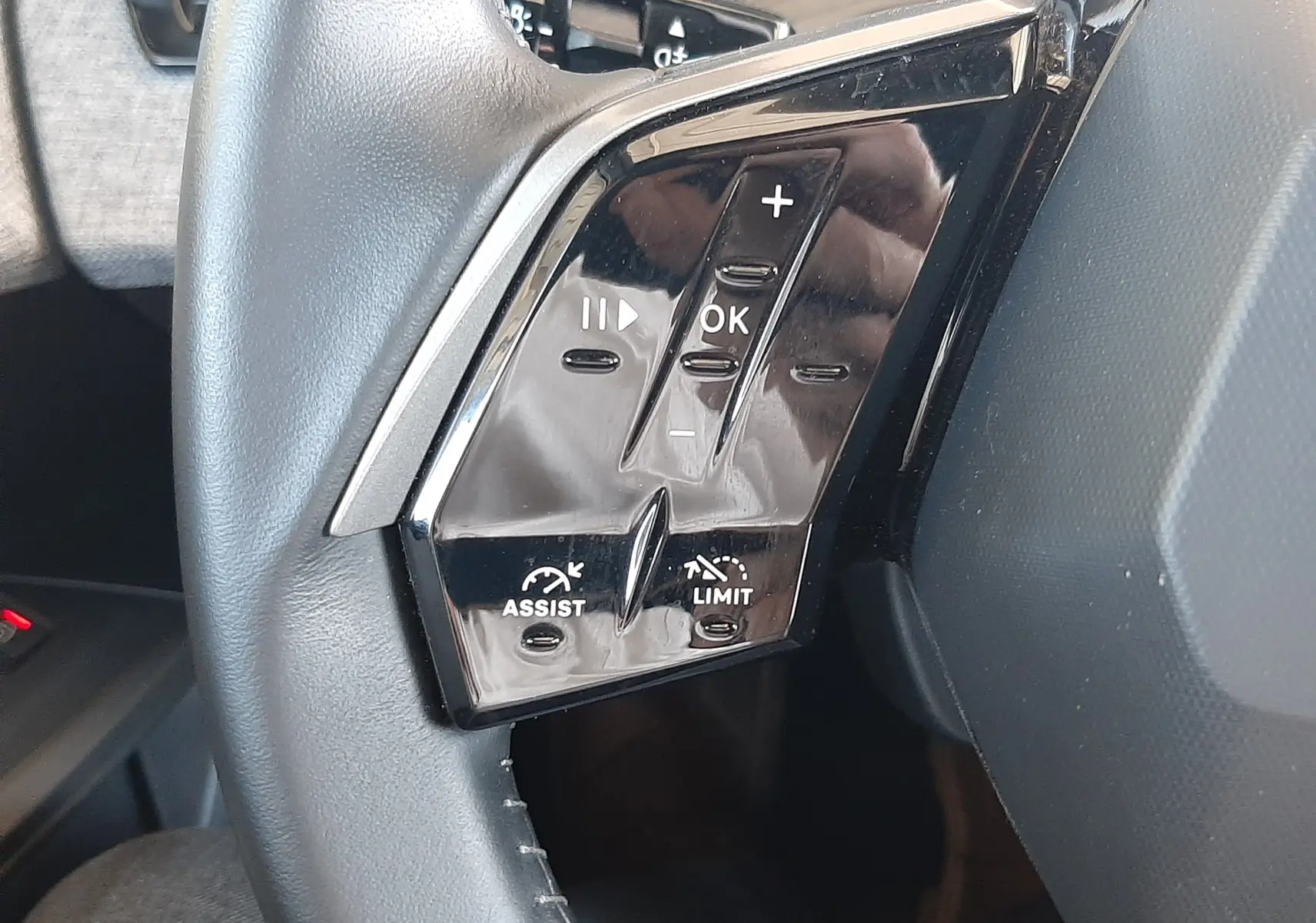 Gros plan sur les commandes gauche du volant noir du Peugeot 5008 Hybrid 2025, boutons de régulateur et limiteur de vitesse.