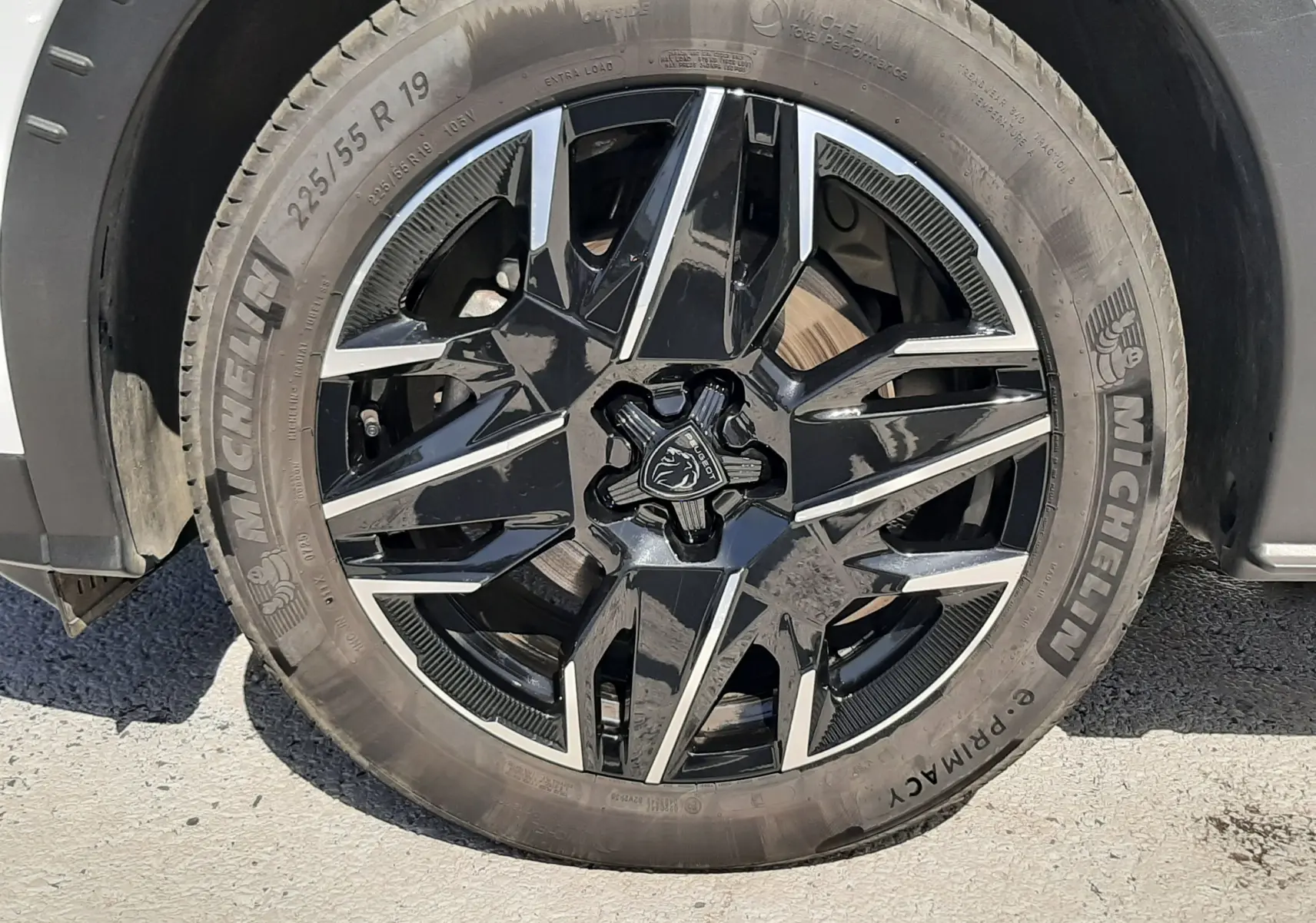 Gros plan sur la roue avant droite blanche d’un Peugeot 5008 Hybrid 2025 avec jante noire brillante au design géométrique.