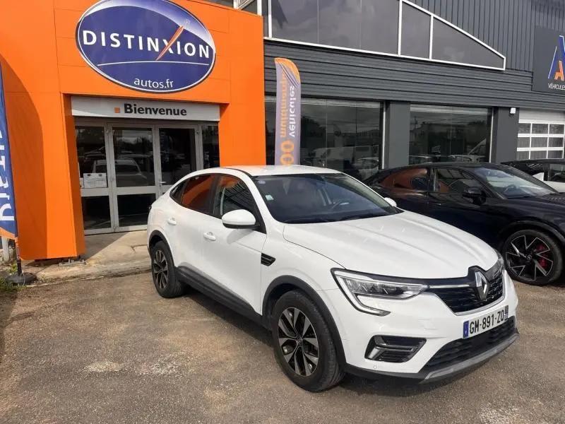 Renault Arkana blanc perle en 3/4 avant droit, avec jantes alu et calandre noire, stationné devant un concessionnaire.