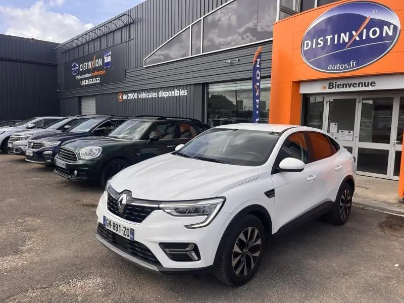 Renault Arkana blanc perle en 3/4 avant droit, avec jantes alu et vitres teintées, devant un concessionnaire Distinxion.