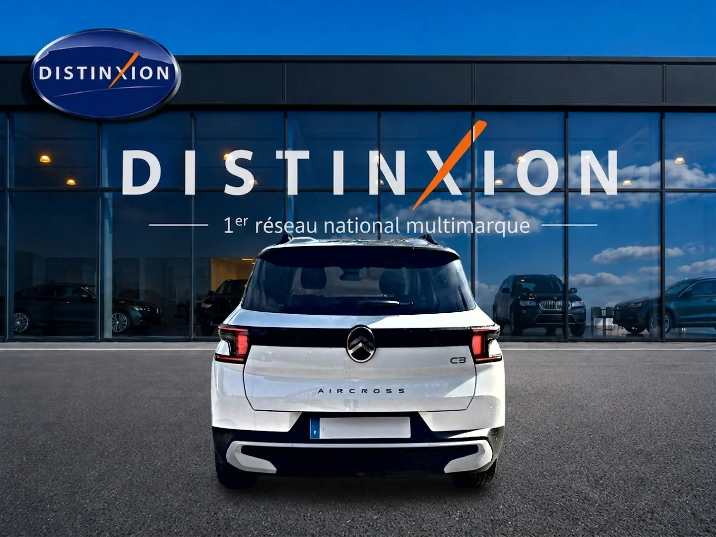 Vue arrière d'un Citroën C3 Aircross blanc garé devant une vitrine avec logo Distinxion.