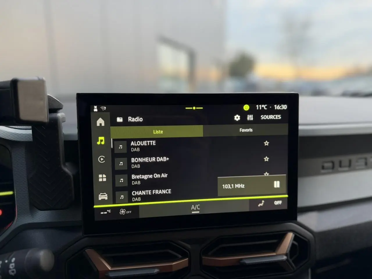 Vue intérieure centrée sur l'écran tactile 10 pouces du Dacia Duster beige Sandstone, avec commandes radio DAB affichées.