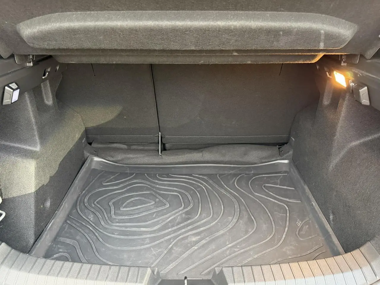 Coffre ouvert du Dacia Duster 2025 beige Sandstone, vue intérieure montrant le tapis de sol en caoutchouc et l'éclairage latéral.