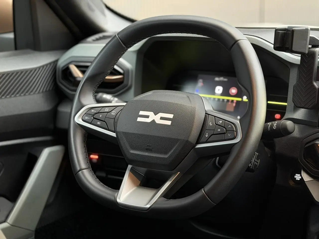 Vue rapprochée du volant noir du Dacia Duster 2025 avec commandes intégrées et tableau de bord digital en arrière-plan.