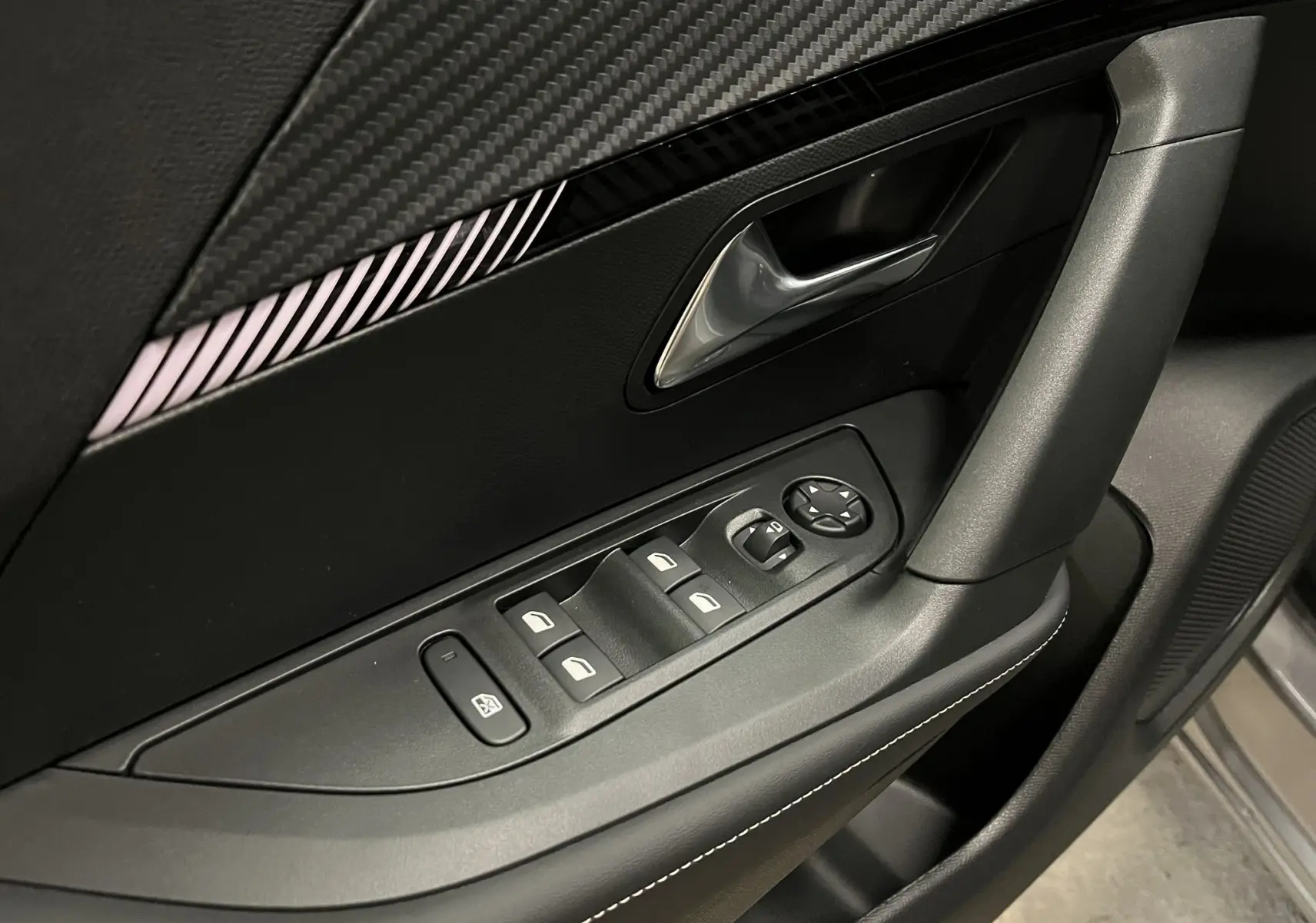 Gros plan sur la commande des vitres et la poignée intérieure côté conducteur du Peugeot 2008 gris, avec finition carbone et surpiqûres blanches.