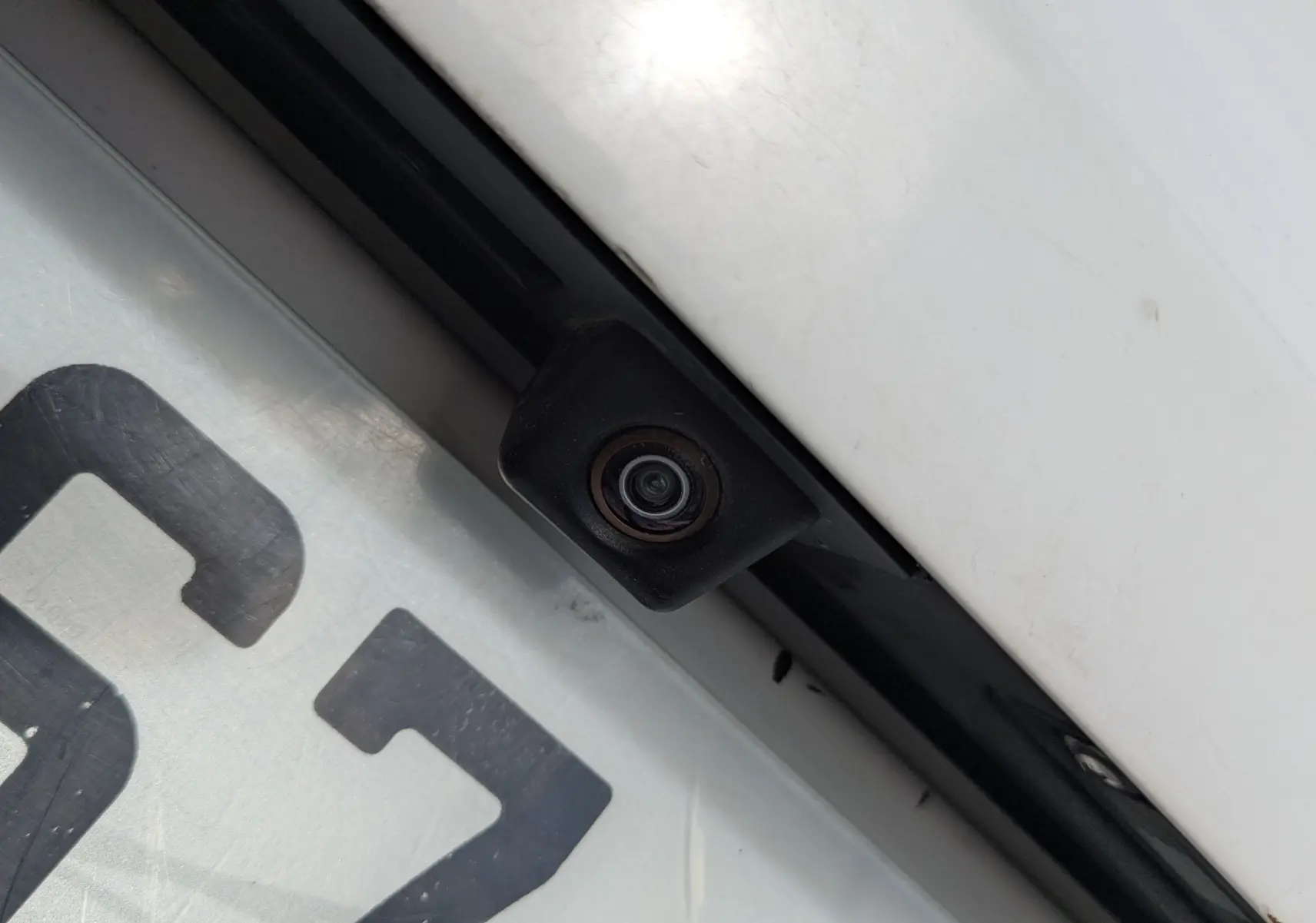 Gros plan sur la caméra de recul noire intégrée au-dessus de la plaque d’immatriculation d’un Volkswagen Tiguan blanc.