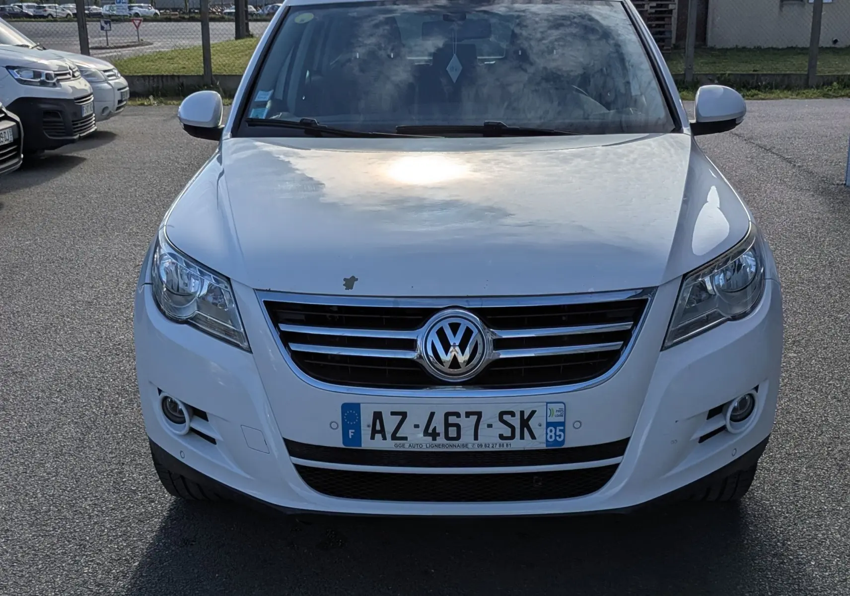 Volkswagen Tiguan blanc vu de face, avec calandre chromée et phares avant allumés au soleil.