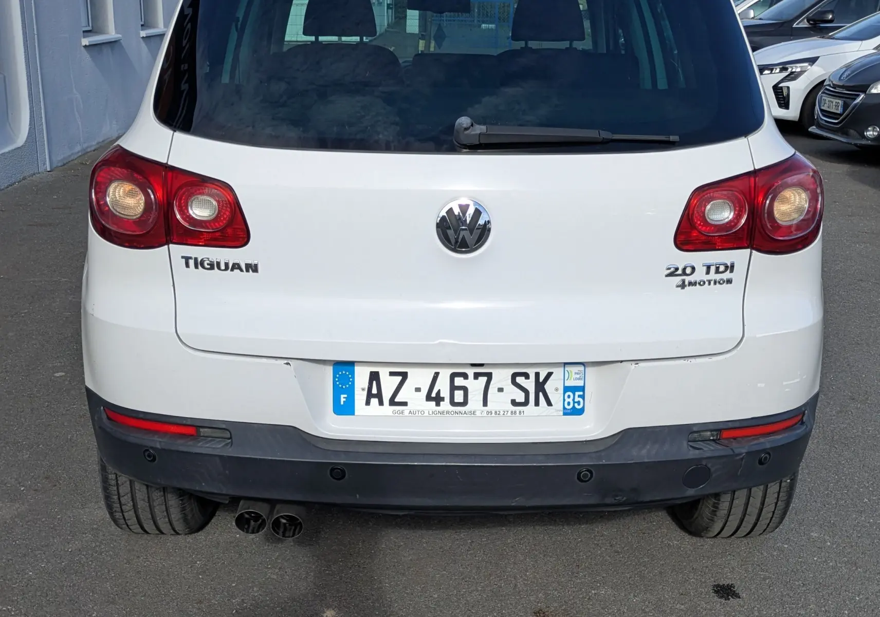 Vue arrière d'un Volkswagen Tiguan blanc avec plaques françaises et feux arrière allumés, stationné en extérieur.