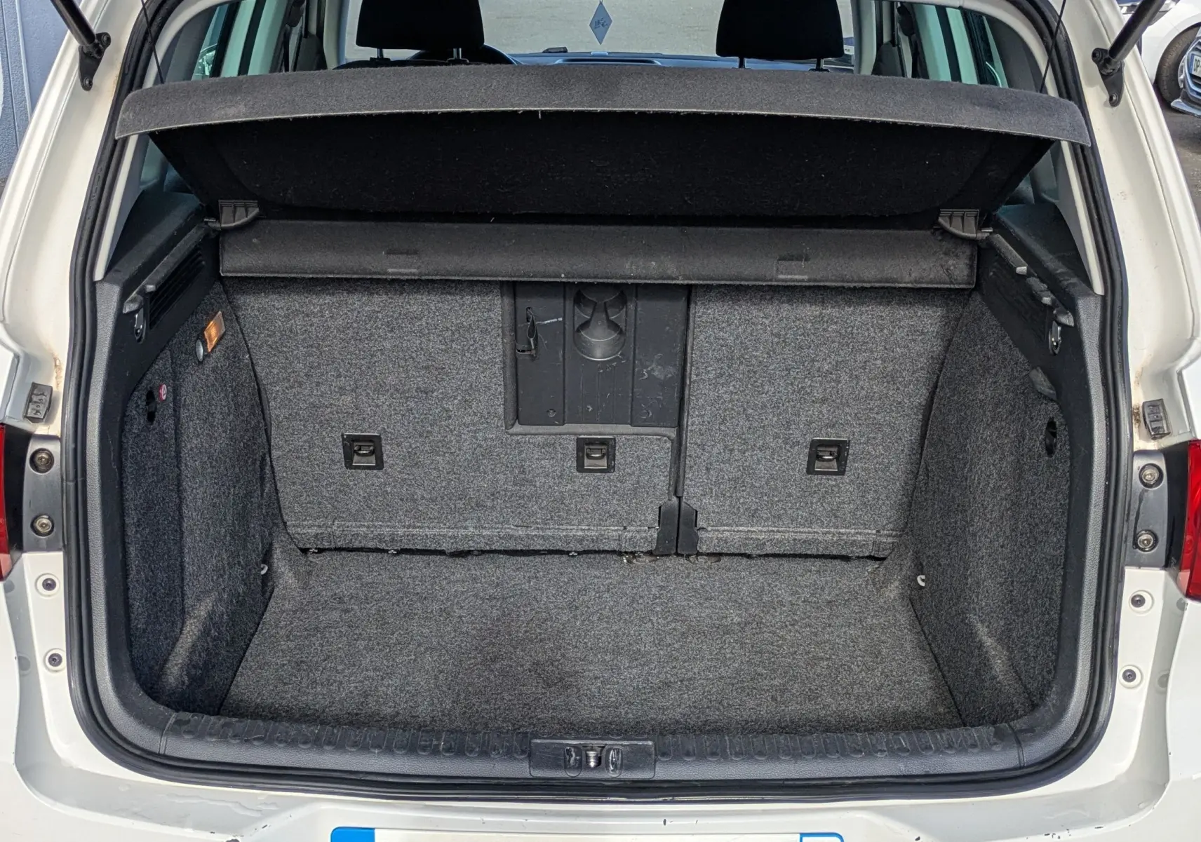 Coffre ouvert vue arrière d'un Volkswagen Tiguan blanc de 2010 avec intérieur de coffre gris et hayon relevé.