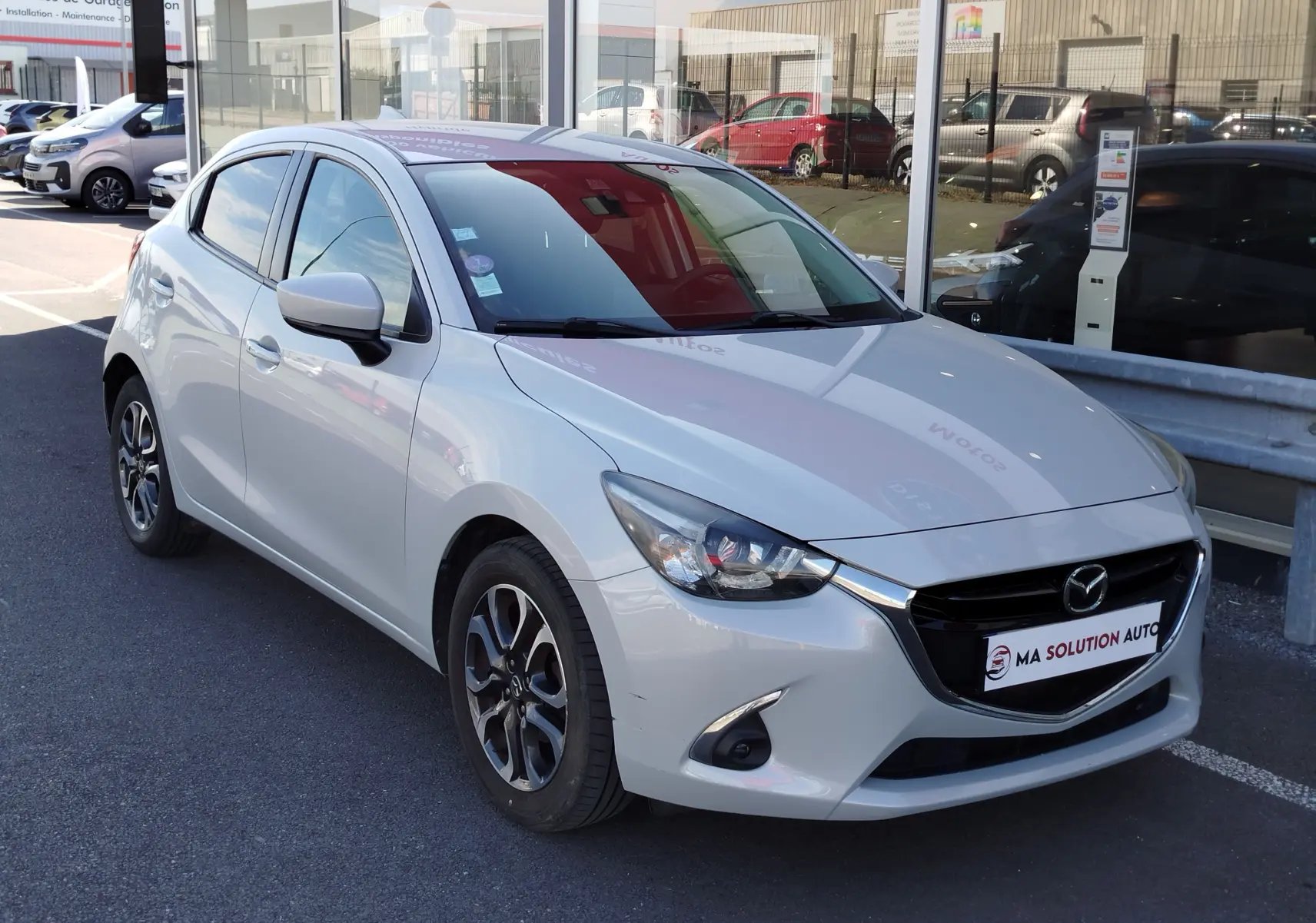 Vue 3/4 avant droite d'une Mazda2 blanche nacrée, avec jantes bi-ton et calandre noire brillante.