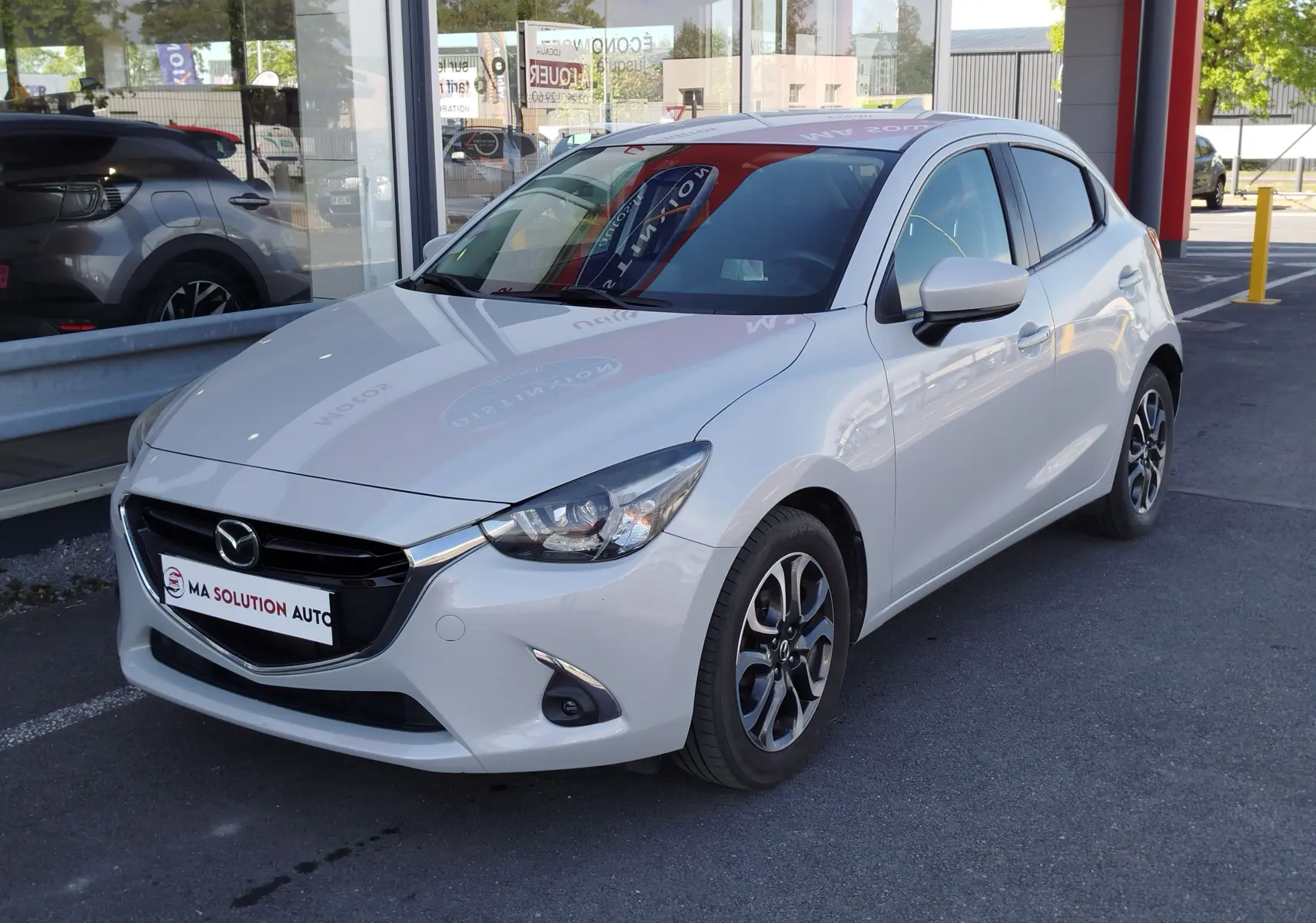 Vue 3/4 avant droit d'une Mazda2 blanche nacrée avec jantes alliage et calandre noire brillante.
