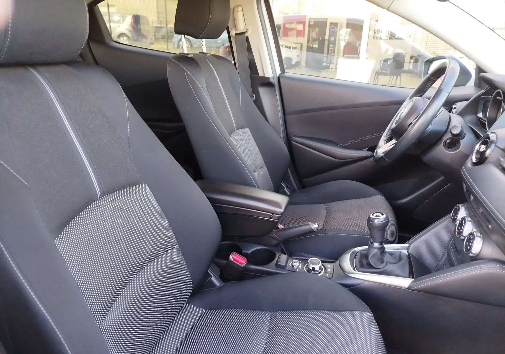 Vue intérieure côté conducteur de la Mazda2 2018 avec sièges tissu noir et console centrale avec boîte manuelle.