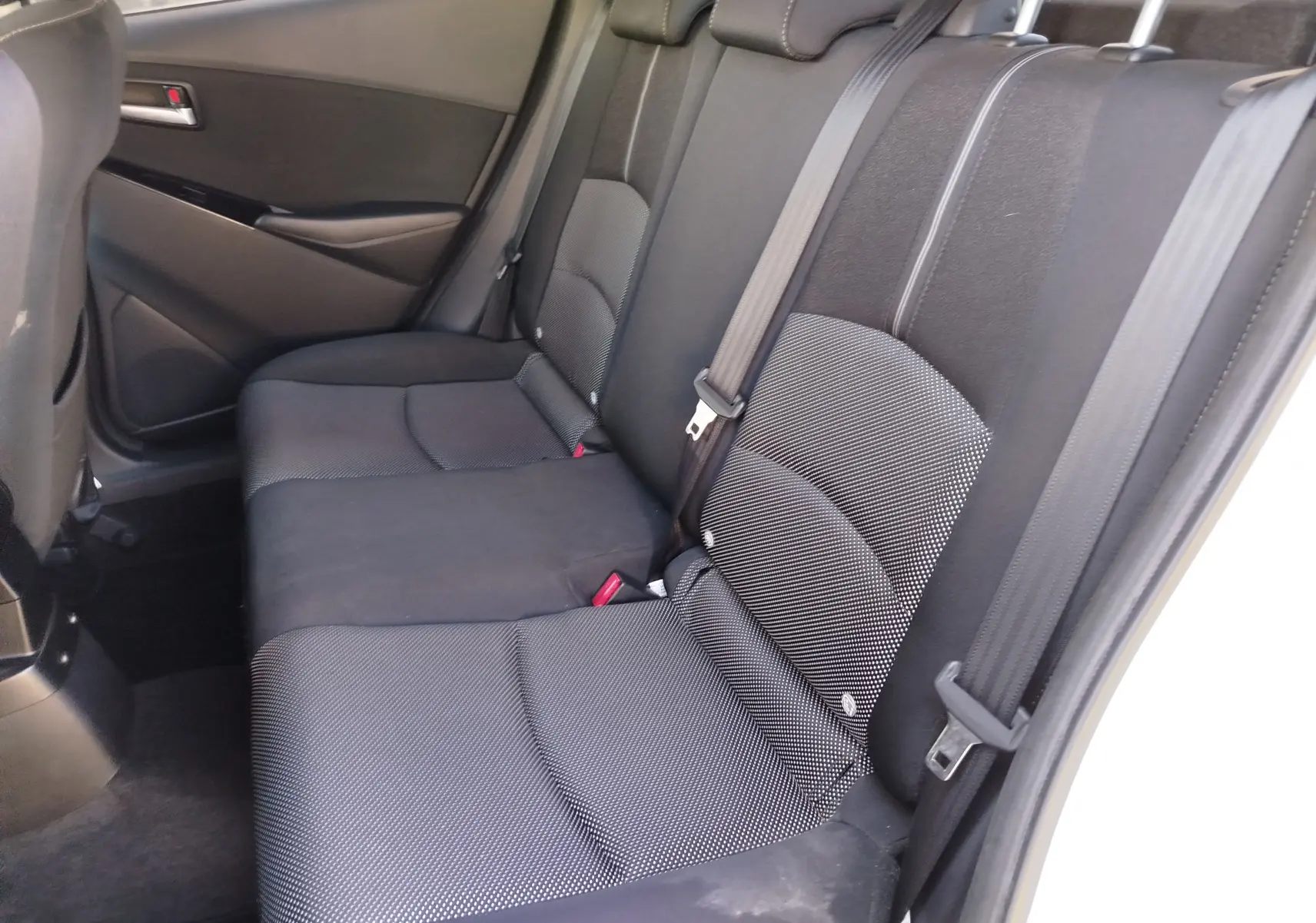 Vue intérieure des sièges arrière noirs en tissu de la Mazda2 2018, côté droit avec ceinture de sécurité visible.