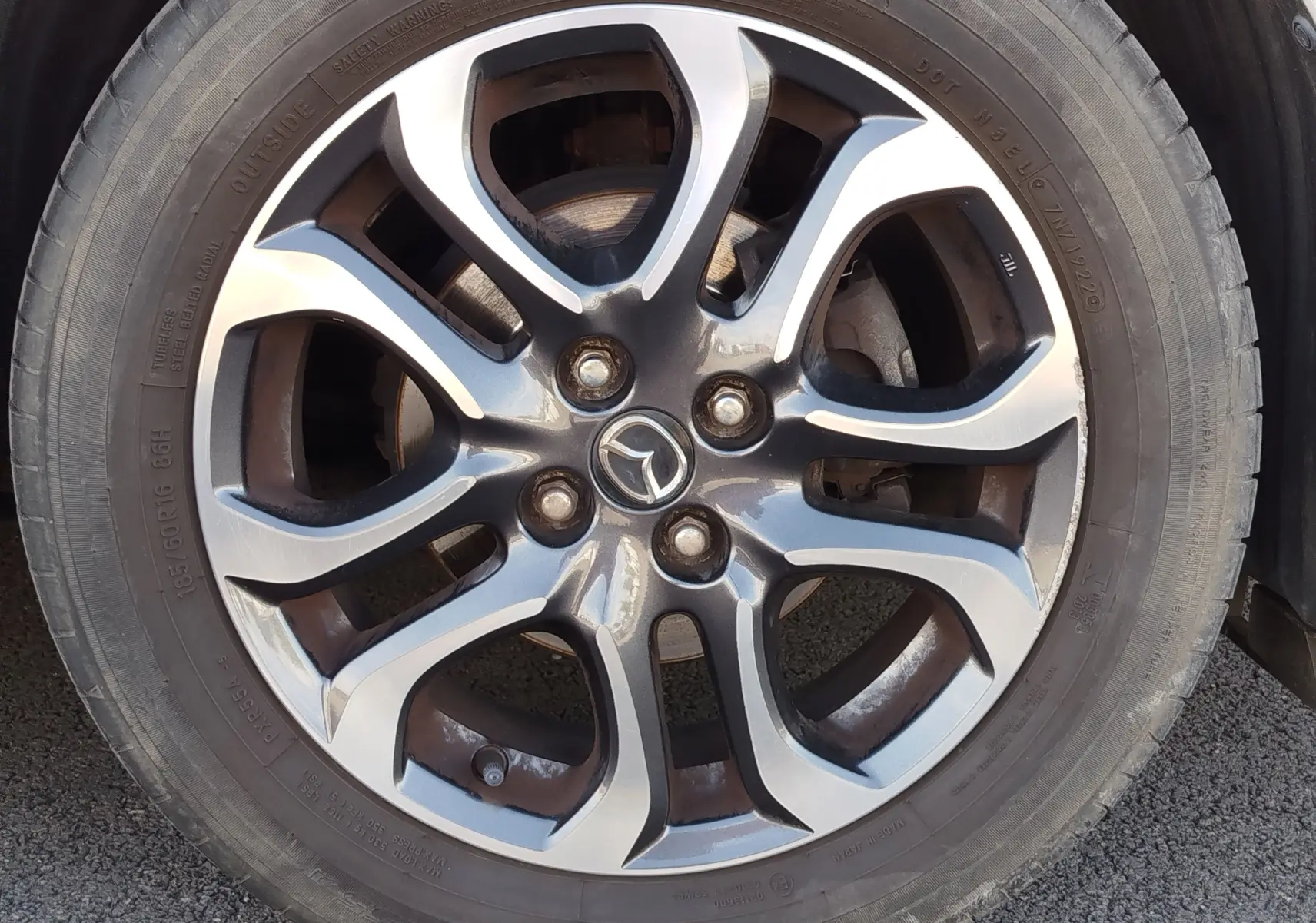 Gros plan sur la roue avant droite d'une Mazda2 blanche avec jante alliage et pneu visible sur sol asphalté.