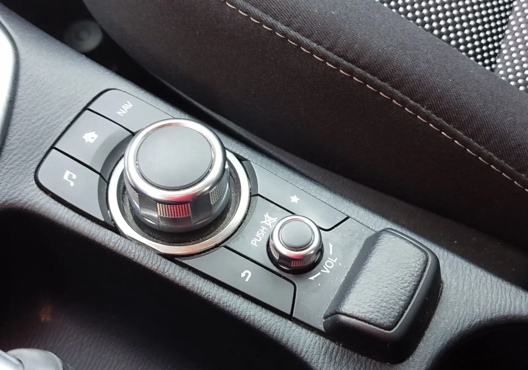 Vue rapprochée du système de commande multimédia central noir sur la console intérieure de la Mazda2 blanche.