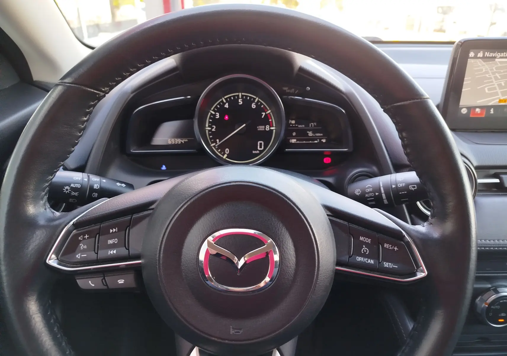 Vue centrée sur le volant noir de la Mazda2 2018 avec tableau de bord et écran de navigation visibles à droite.