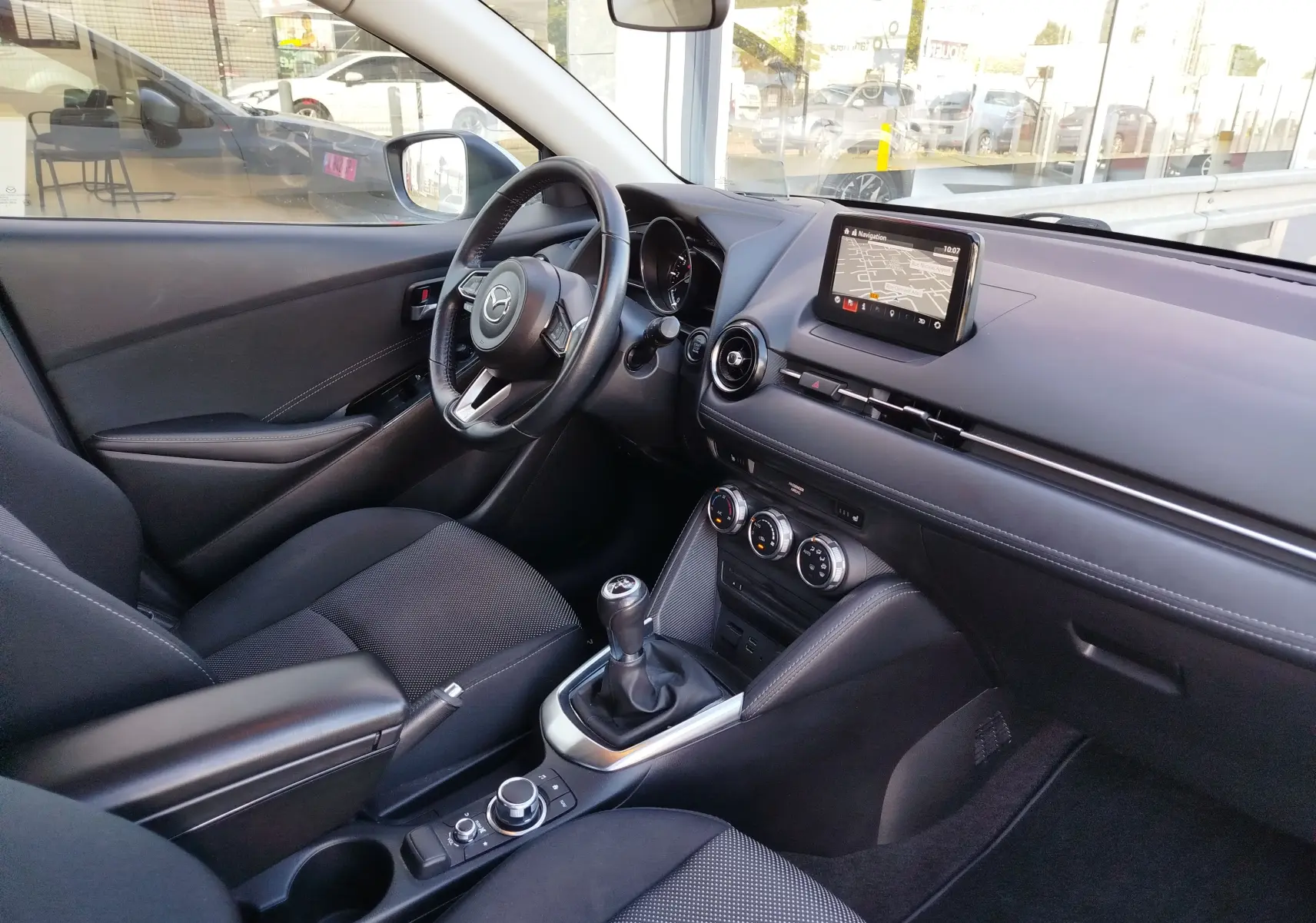 Vue intérieure côté conducteur de la Mazda2 2018 avec tableau de bord noir et écran tactile central affichant la navigation.