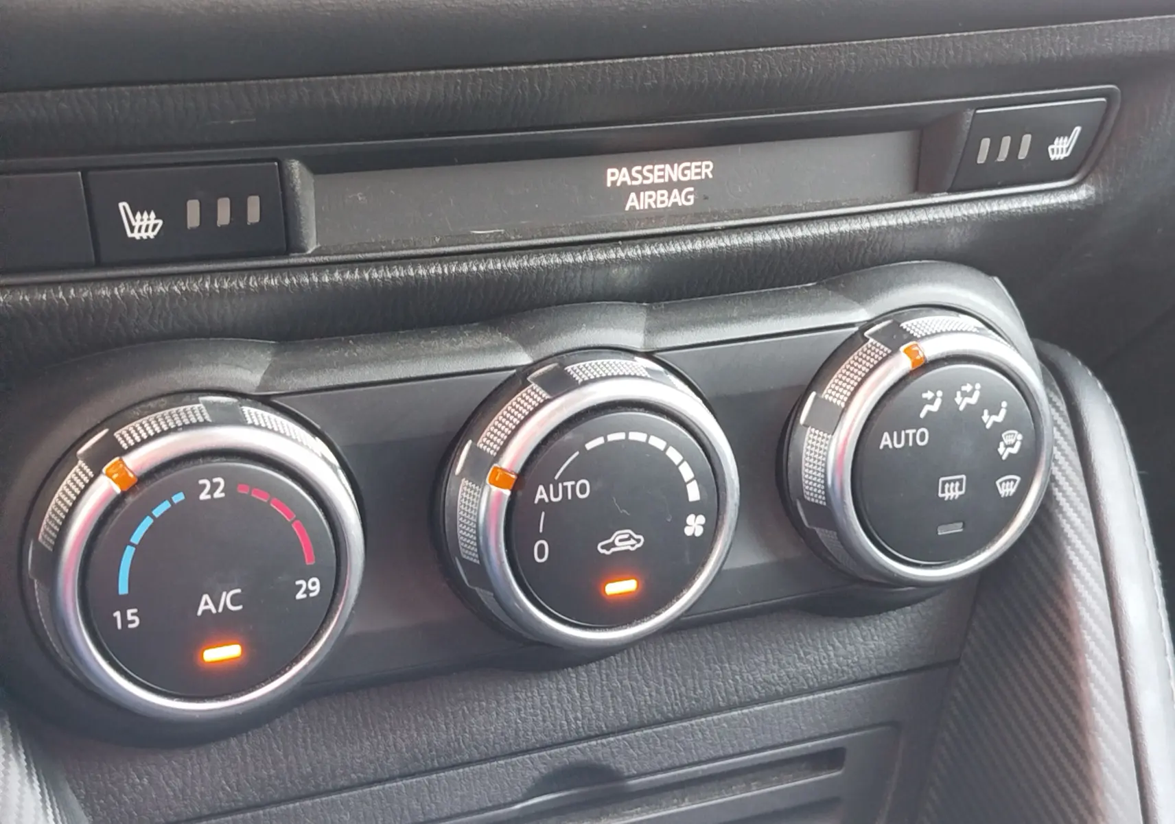 Gros plan sur les commandes de climatisation automatique et sièges chauffants du tableau de bord d'une Mazda2 2018.