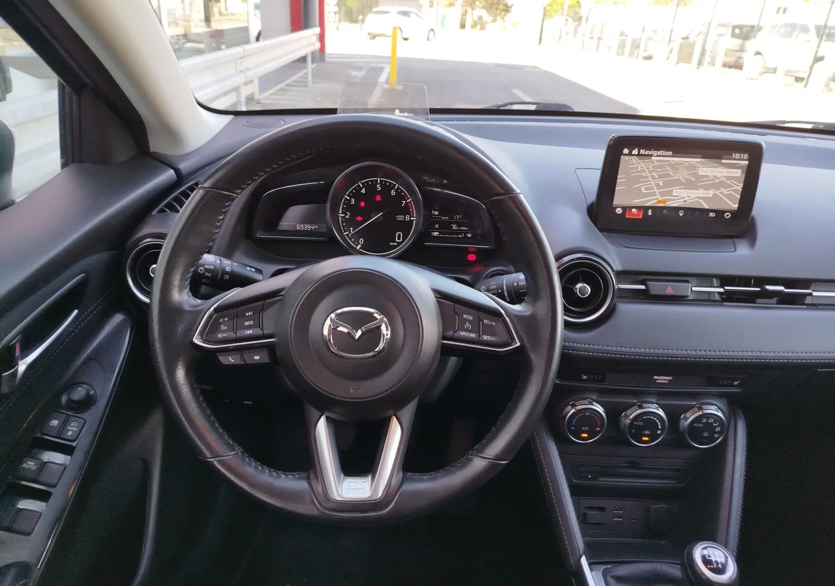Vue intérieure centrée sur le volant cuir et le tableau de bord avec écran de navigation de la Mazda2 blanche.